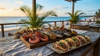 Fresh seafood platter with grilled shrimp and fish tacos served on wooden table at beachfront restaurant during golden hour sunset with ocean view.