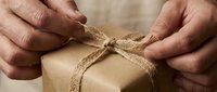 Hands tying natural twine around kraft paper wrapped gift box, showing eco-friendly packaging and sustainable gift wrapping technique for retail and holiday commerce.