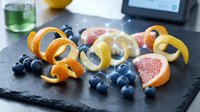 Fresh citrus peels with blueberries on dark slate board for healthy snacking and culinary garnish preparation in modern kitchen setting.