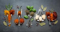 Aromatic spices and herbs arranged in vintage spoons on dark slate background. Culinary ingredients for cooking and seasoning food preparation.