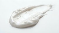 Creamy white cosmetic product smear or moisturizer texture on white background for skincare, beauty, and cosmetics marketing purposes.