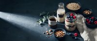 Healthy breakfast ingredients with oats, berries, nuts and milk on dark background. Nutritious morning meal preparation concept for wellness lifestyle.