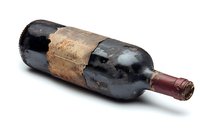 Old dusty wine bottle with worn label and aged patina lying on white background, isolated vintage alcoholic beverage showing signs of long-term cellar storage.