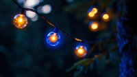 Glowing string lights create magical bokeh effect against dark evening background, blue and orange illuminated bulbs cast warm ambient glow outdoors.