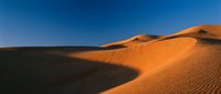 Vast desert landscape with golden sand dunes under clear blue sky, showcasing natural patterns and shadows for travel, nature, and environmental design projects.