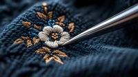 Delicate floral embroidery detail on dark blue fabric with metallic needle in macro shot, showcasing intricate needlework craftsmanship and traditional stitching technique.