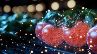 Red Christmas ornaments with sparkling glitter texture against blurred evergreen branches and golden bokeh lights create magical holiday atmosphere.