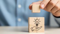 Businessman hand placing wooden cube with lightbulb and hand icon representing innovation and creative business solutions concept.