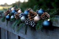 Festive winter decoration with blue and silver ornaments, frosted pinecones and fresh evergreen branches arranged on wooden railing for holiday season.