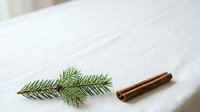 Cinnamon sticks and fresh evergreen sprigs arranged on white marble surface for holiday cooking and seasonal decoration projects.