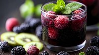 Fresh berries and kiwi slices float in dark purple sangria cocktail garnished with mint leaves, served in rocks glass against dark background.