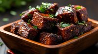 Juicy grilled pork belly chunks glazed with sweet and spicy sauce, garnished with fresh herbs in wooden bowl on dark background. For food blogs and menus.