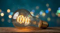 Vintage Edison bulb with glowing filament on wooden surface against blurred city lights background, symbolizing creativity and innovation in modern business.