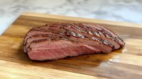 Sliced medium rare flank steak on wooden cutting board shows juicy pink center and charred exterior with visible seasoning and grill marks for food photography.