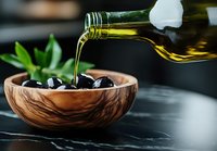 Pouring extra virgin olive oil into wooden bowl with black olives, close-up view on dark background with green leaves, Mediterranean cuisine concept.