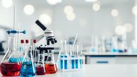 Laboratory equipment with microscope and colorful chemical solutions in glass flasks for scientific research and medical testing in modern lab.