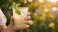 Refreshing lemonade or mojito cocktail with fresh mint leaves and ice held in hand outdoors during golden hour, perfect for summer beverages and drink photography.