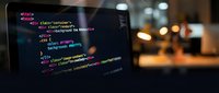 Web developer coding HTML CSS on laptop screen with colorful syntax highlighting in dark office environment for programming projects and software development.