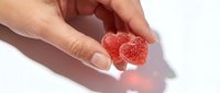 Close-up of hand holding red gummy candy hearts with sugar coating on white background. Suitable for confectionery, candy, sweets, and food advertising projects.