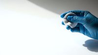 Medical professional hand in blue latex glove holding white pill or tablet against clean white background for healthcare and pharmaceutical use.
