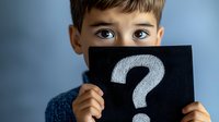 Young boy holding black card with white question mark symbol, showing only eyes above, expressing curiosity and wonder against blue background.