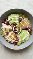 Fresh fruit platter with sliced apples, grapes, pomegranate seeds and nuts arranged in decorative spiral pattern on gray plate for healthy snacking and entertaining.