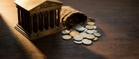 Banking crisis concept with miniature bank building and scattered coins on wooden surface representing financial instability and economic collapse.