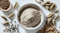 Organic cardamom powder in stone bowl with whole green pods and seeds scattered on white background. Natural spice ingredients for cooking.