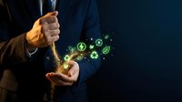 Businessman in suit holding glowing green eco-friendly icons representing sustainable technology, renewable energy and environmental conservation concepts.
