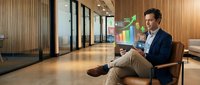Professional Asian businessman in modern office lobby using tablet with holographic data visualization interface for business analytics and digital transformation.