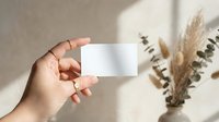 Hand holding blank white business card mockup with dried pampas grass and eucalyptus branches in soft natural lighting for branding presentation.
