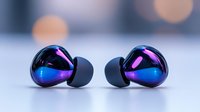 Modern wireless earbuds with holographic iridescent finish displaying purple and blue reflections on clean surface with bokeh background lighting effects.