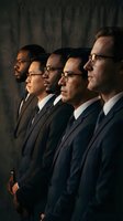 Five diverse professional businessmen in dark suits standing in profile formation against dramatic lighting for corporate leadership concepts.