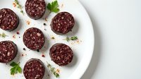 Dark chocolate salami slices with nuts arranged on white plate, garnished with fresh herbs and spices for gourmet appetizer presentation.