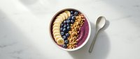 Acai bowl with sliced banana, blueberries, and granola in white bowl on marble surface, overhead view for food blogging and healthy eating content.