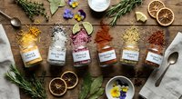Colorful spice collection in glass jars with herbs and dried orange slices on rustic wooden background for culinary cooking and seasoning recipes.