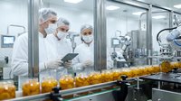 Three pharmaceutical workers in protective gear monitoring automated production line with orange bottles in sterile manufacturing facility.