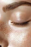 Close-up of glowing skin with natural freckles, closed eye, and groomed eyebrow showing dewy complexion and radiant skincare results.