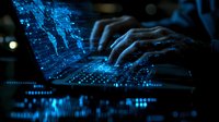 Hands typing on laptop keyboard with glowing blue digital data visualization and network connections, dark atmospheric lighting creates cybersecurity mood.