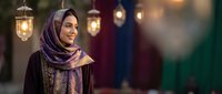 Young Middle Eastern woman in purple hijab smiling warmly during evening celebration with traditional lanterns creating atmospheric lighting backdrop.