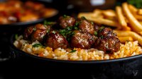 Savory meatballs with herbs served over rice in cast iron skillet, comfort food meal with golden fries, homestyle cooking for restaurant menu design.