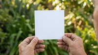 Mature hands holding blank white card against lush green foliage background, suitable for advertising, marketing mockups, greeting cards, and promotional campaigns.
