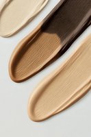 Foundation makeup swatches in different skin tone shades from light to dark brown showing creamy texture and smooth application strokes on white background.