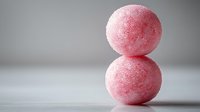 Pink sugar-coated candy balls stacked on white surface against neutral gray background, showcasing sweet confectionery texture for food marketing.