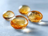 Amber liquid gel capsules with tiny bubbles on gray surface, macro photography showing transparent medicine pills in warm golden color with soft focus.