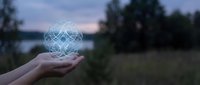 Hand holding glowing geometric heart symbol with interconnected lines floating above palm against blurred natural landscape at twilight for wellness concepts.