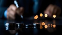 Stacks of coins in dark setting with blurred business person and bokeh lights background, representing financial planning and investment strategy.