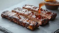 Grilled barbecue ribs with glossy sauce on slate board. Smoky pork ribs glazed with tangy barbecue sauce, perfect for summer cookouts and restaurant menus.