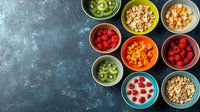 Fresh breakfast ingredients in colorful ceramic bowls on dark background. Healthy morning meal with granola, berries, fruits and yogurt for balanced diet.