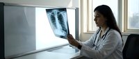 Female doctor examining chest X-ray film in modern medical office for lung health diagnosis and respiratory care consultation.